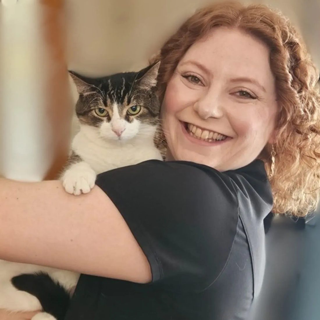 Smiling woman with curly hair holding a tabby cat