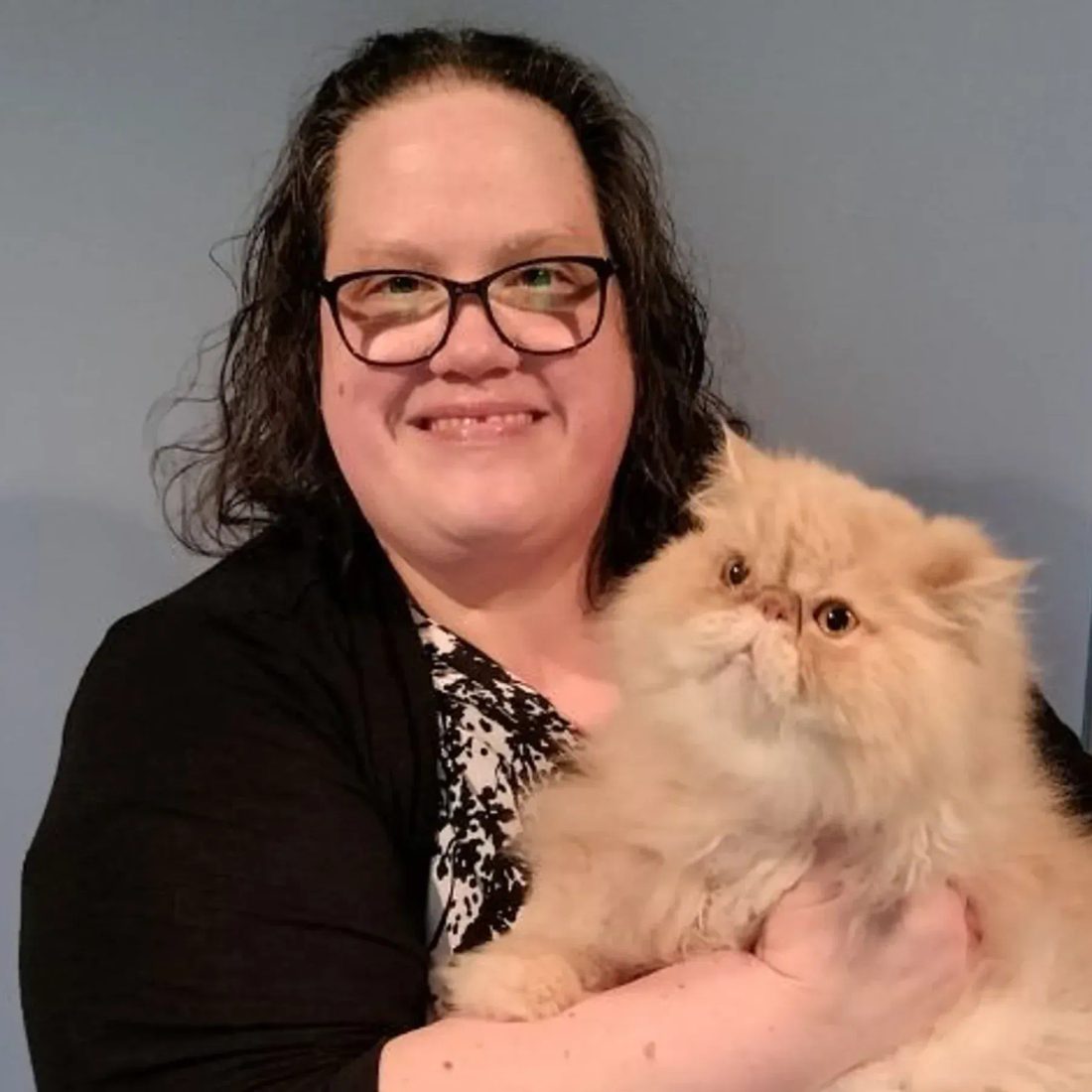 Smiling woman with glasses holding a fluffy orange cat