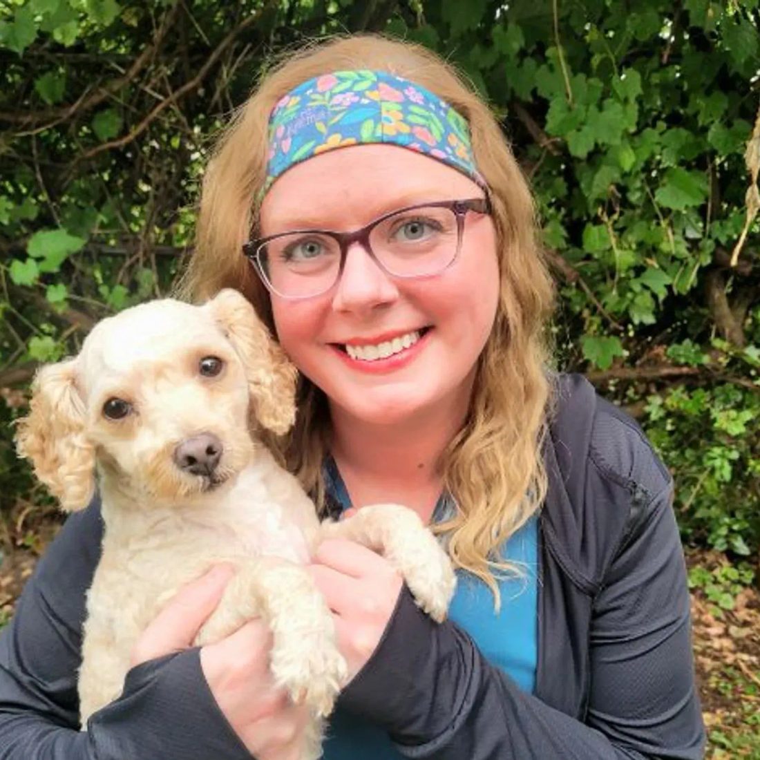 Woman with glasses and headband holding a small white dog outdoors